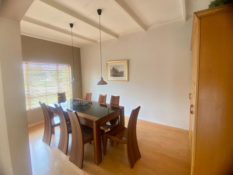 A dining room featuring laminate flooring, exposed beam ceiling, and pendant lighting, providing a functional space for family meals.