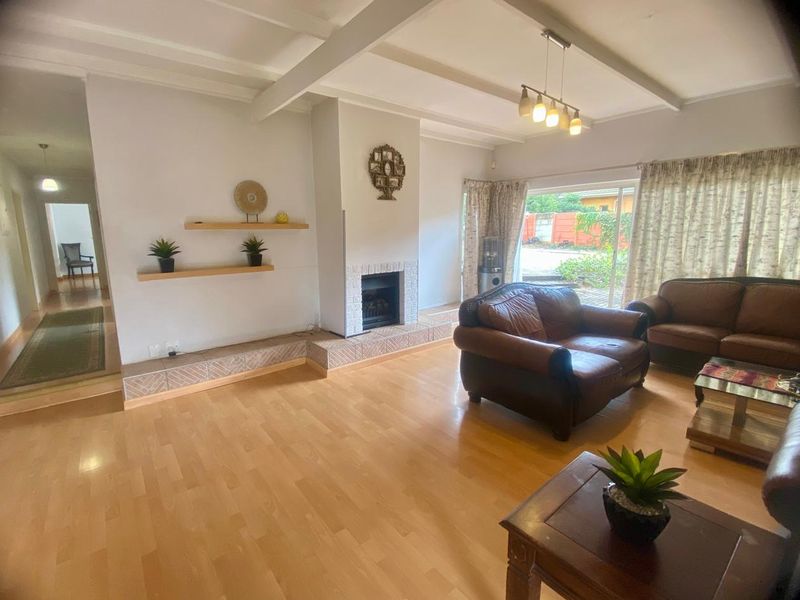 Spacious living room featuring laminate flooring, a central fireplace with tiled hearth, exposed ceiling beams, and direct access to the garden via sliding doors.
