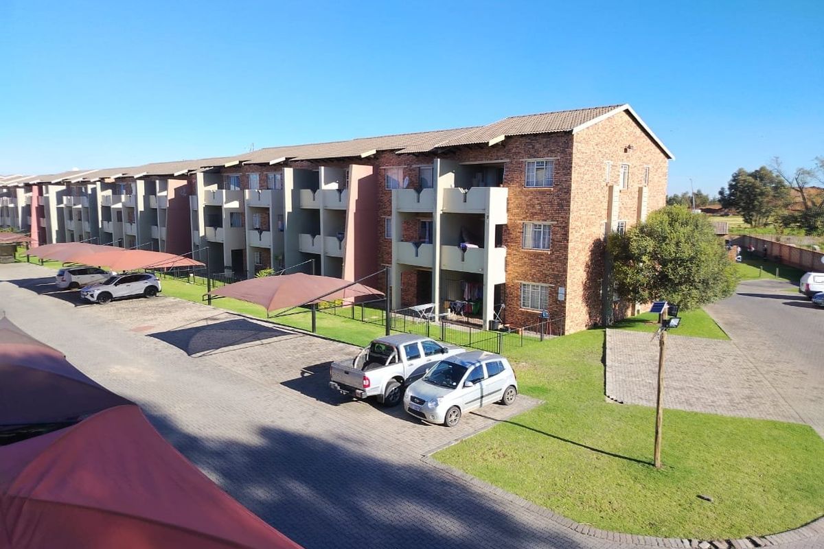 Aerial view of a multi-story brick apartment complex featuring covered parking bays, landscaped lawns, and private balconies for each unit.