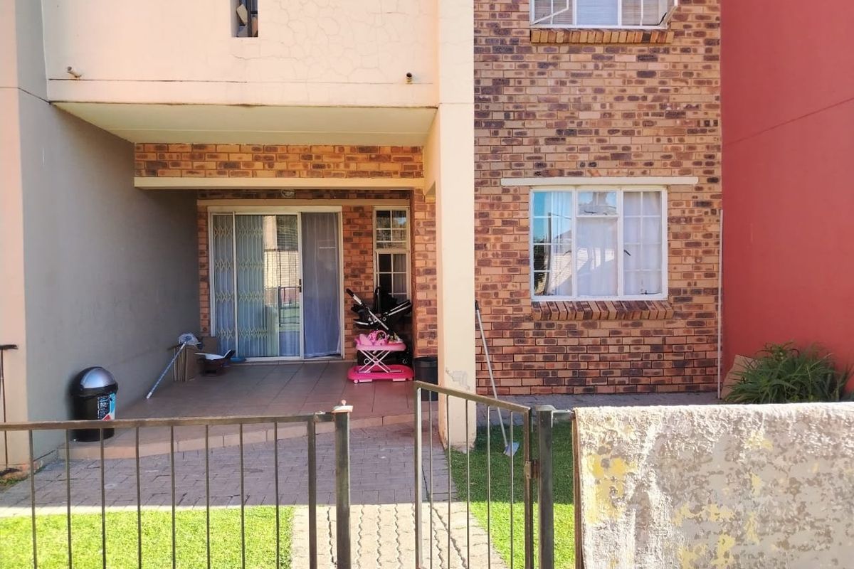 Exterior view of an apartment unit featuring a paved patio area, brick facade, and a small private garden space with metal fencing.
