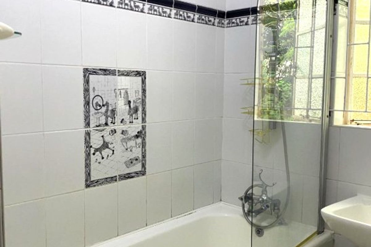 A functional bathroom featuring a bathtub with a glass shower screen, wall-mounted shower mixer, and decorative tiled accents.
