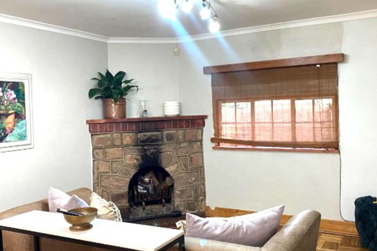 A living room featuring a stone-clad corner fireplace, parquet wood flooring, and a window with a wooden blind.