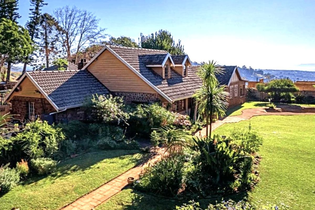A charming rear elevation of a house featuring stone and timber cladding, a tiled roof with dormer windows, and a well-maintained landscaped garden.