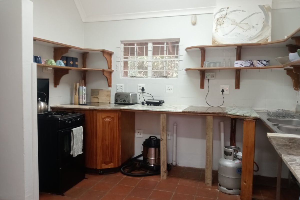 A functional kitchen area featuring open timber shelving, a freestanding stove, marble-look countertops, and a double bowl sink with tiled flooring.