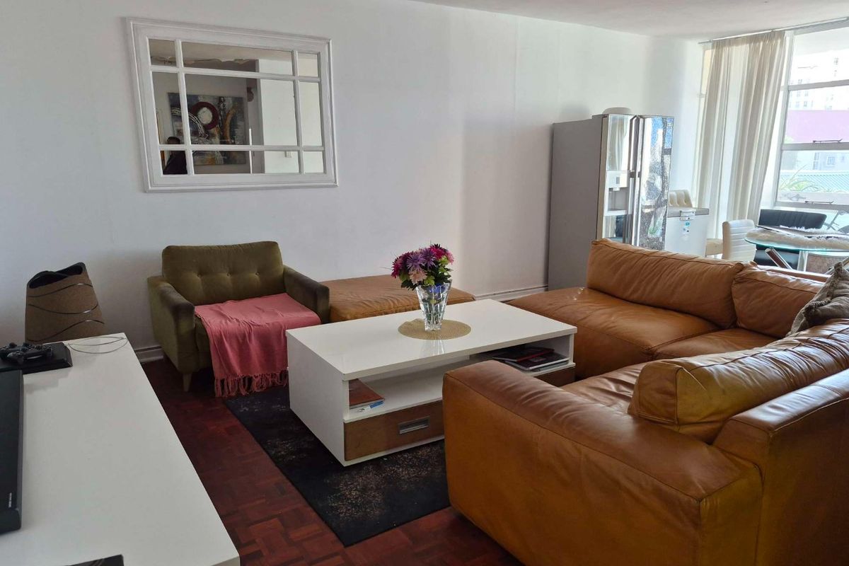 A spacious living room featuring classic parquet flooring and large windows that provide ample natural light, creating a comfortable and inviting atmosphere.