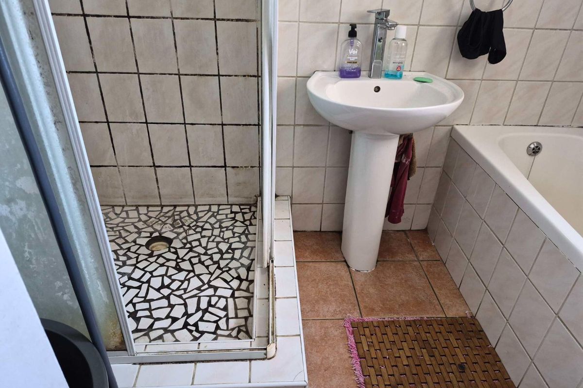 A functional bathroom featuring a pedestal basin, bathtub, and a separate shower enclosure with tiled finishes throughout.