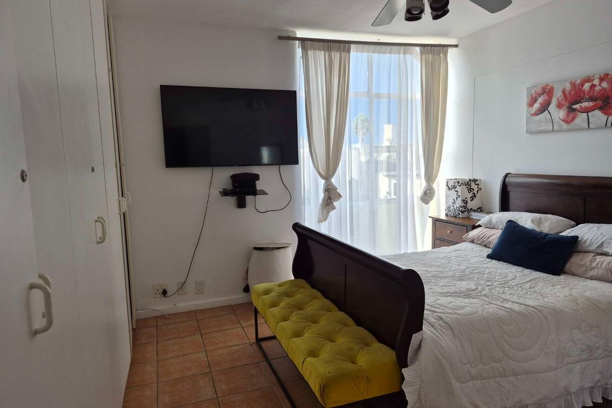 A bedroom featuring built-in cupboards, tiled flooring, and a ceiling fan, with natural light provided by a large window.