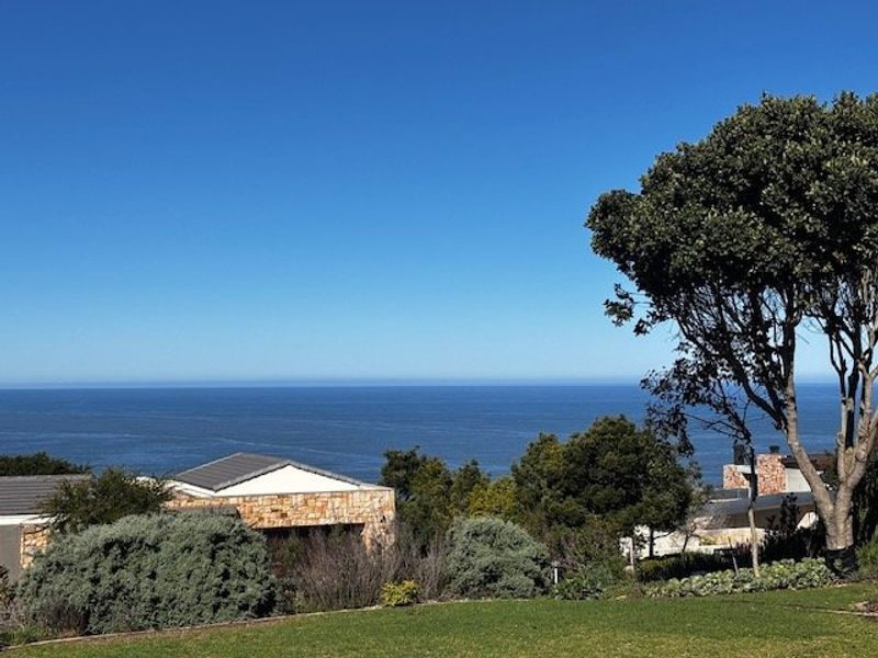 A scenic view overlooking the ocean with established garden landscaping and glimpses of nearby residential architecture.