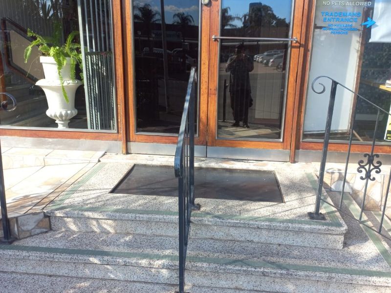 Main building entrance featuring timber-framed glass doors, terrazzo steps, and a metal handrail, providing access to the apartment complex.