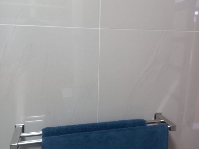 A close-up view of a bathroom wall featuring modern light-colored ceramic tiles and a polished chrome double towel rail.