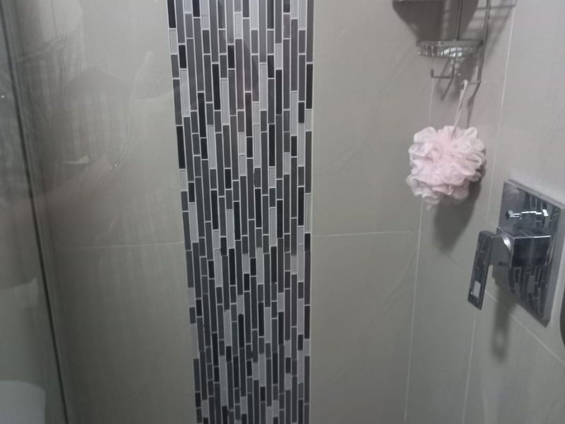 A modern shower enclosure featuring a decorative mosaic tile accent strip, chrome mixer tap, and glass screen.