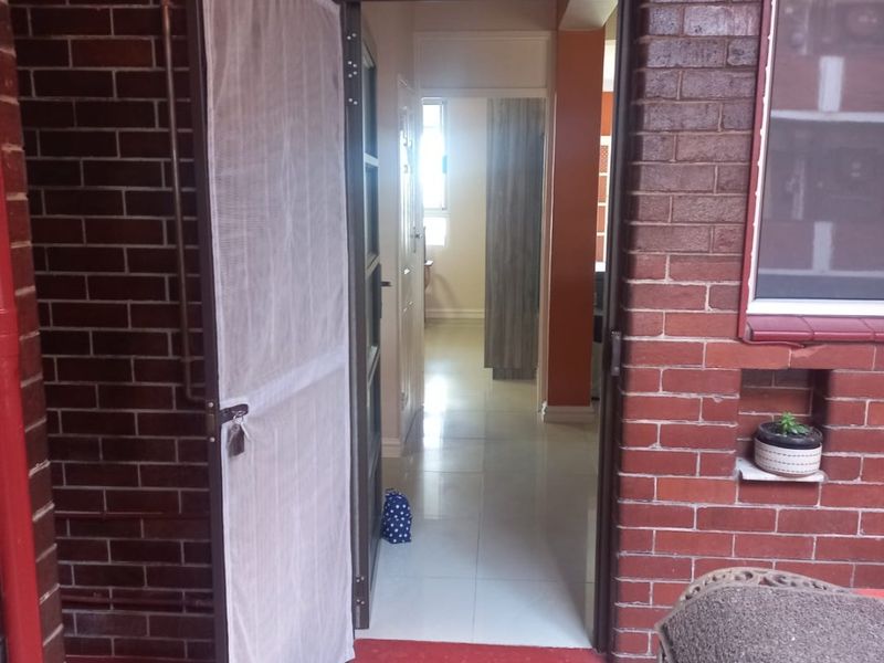 Entrance area featuring exposed brickwork, a security screen door, and tiled flooring leading into the apartment interior.