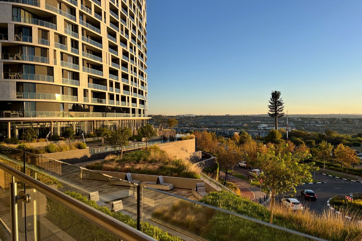 A high-rise apartment building exterior featuring a landscaped terrace with glass balustrades and expansive views of the surrounding neighborhood.