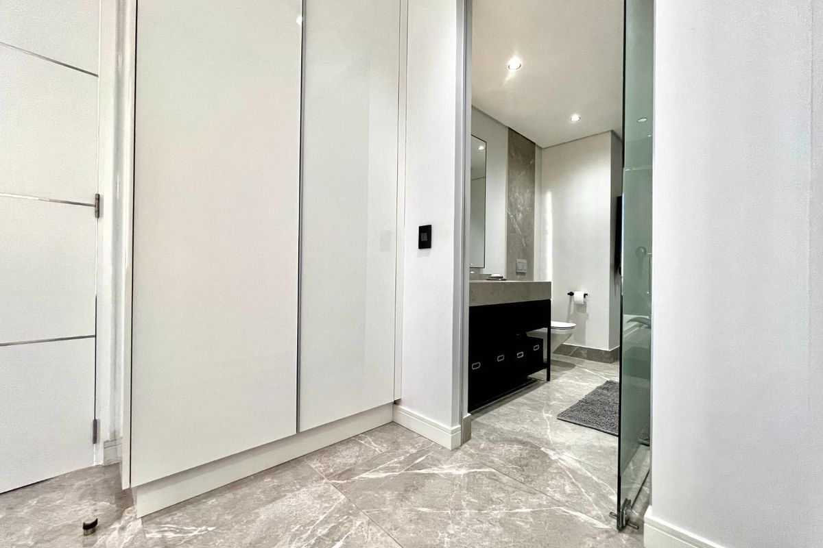 Modern bathroom featuring high-end marble-look tiling, sleek built-in cabinetry, and a glass entry door, presenting a clean and contemporary aesthetic.