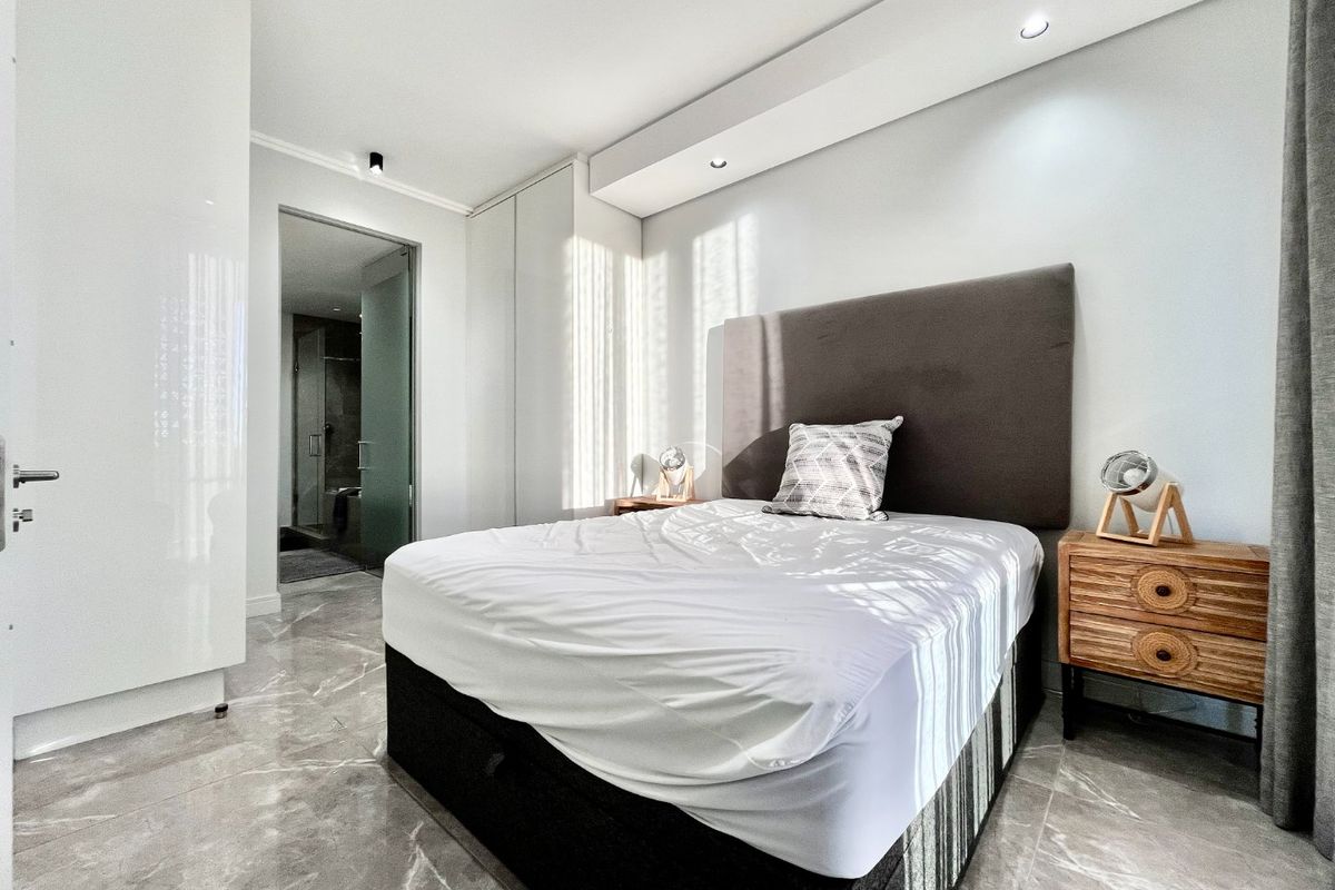 Modern bedroom featuring high-gloss built-in cupboards, elegant marble-look floor tiles, recessed ceiling lighting, and direct access to an en-suite bathroom.