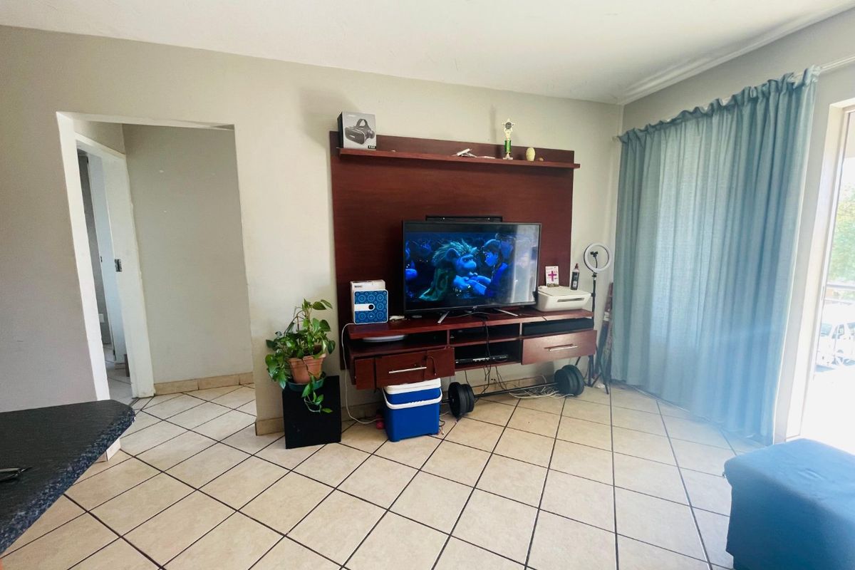 A living room featuring tiled flooring and a built-in media unit, with access to an outdoor area through a sliding door.