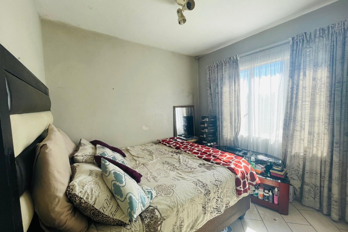 A bedroom featuring tiled flooring and natural light through window curtains. The space requires cosmetic updates including wall repairs and fresh paint.