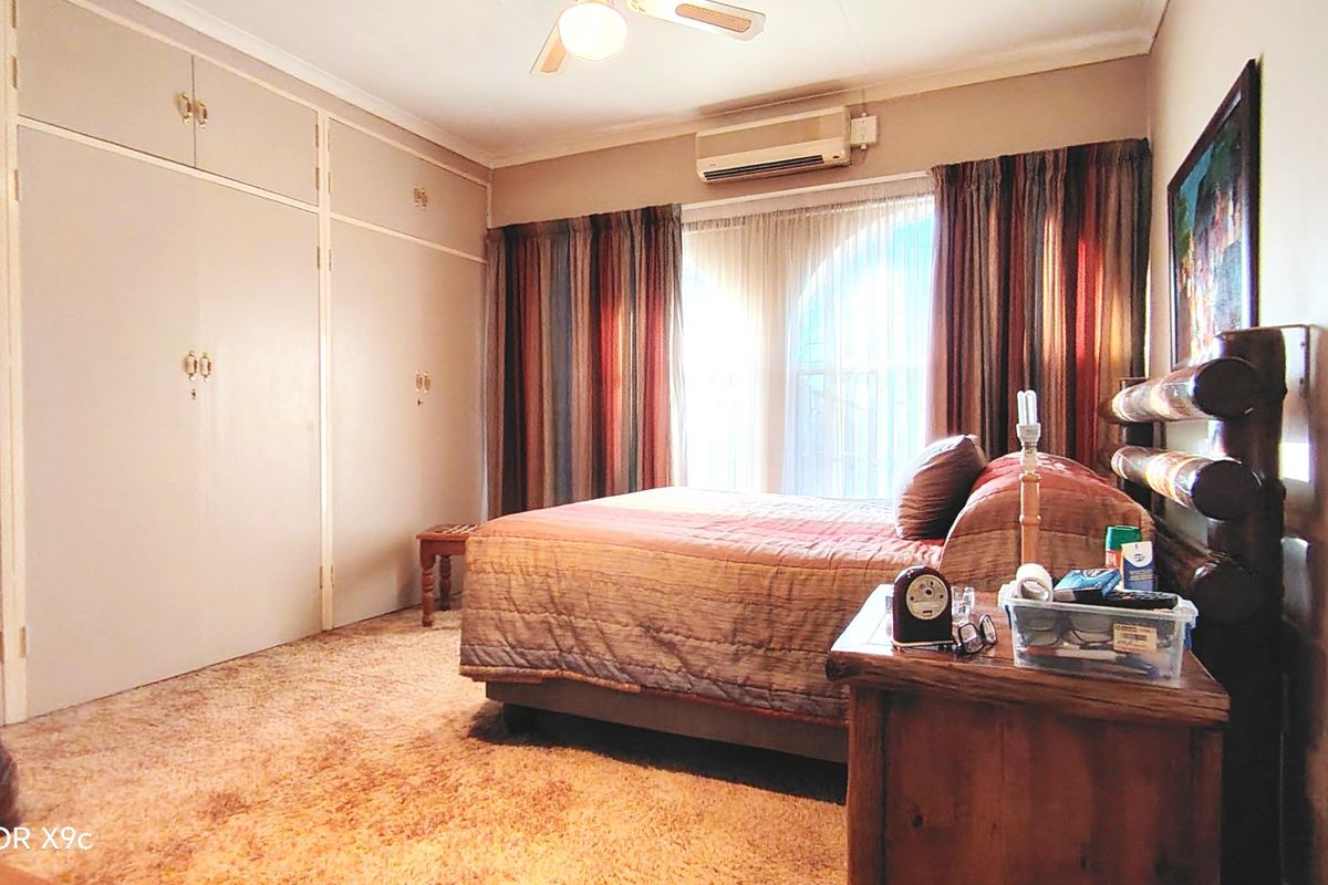 A bedroom featuring built-in cupboards, a ceiling fan, and a wall-mounted air conditioning unit, with carpeted flooring throughout.