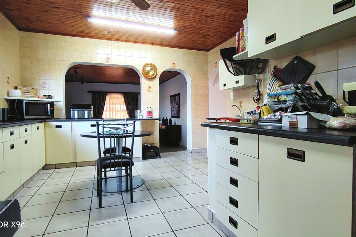 A functional kitchen featuring tiled flooring, timber ceiling, and built-in cabinetry with laminate countertops, connected to adjacent living spaces via arched doorways.