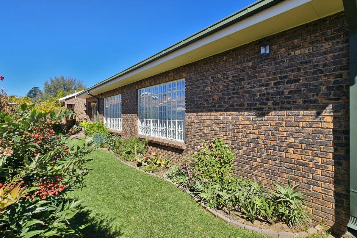 A view of the rear exterior of the townhouse featuring a face brick facade, security-barred windows, and well-maintained garden landscaping.