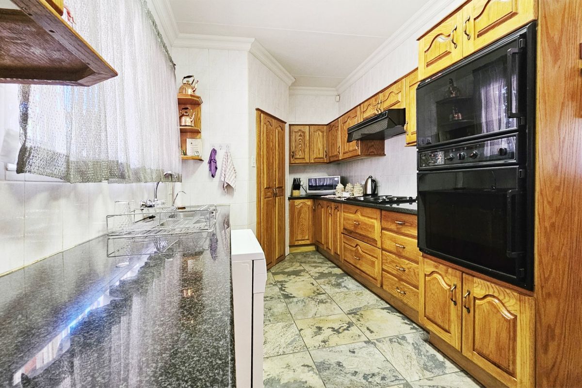 A functional kitchen featuring traditional wooden cabinetry, granite countertops, a double wall oven, and tiled flooring, offering a classic layout with ample storage space.