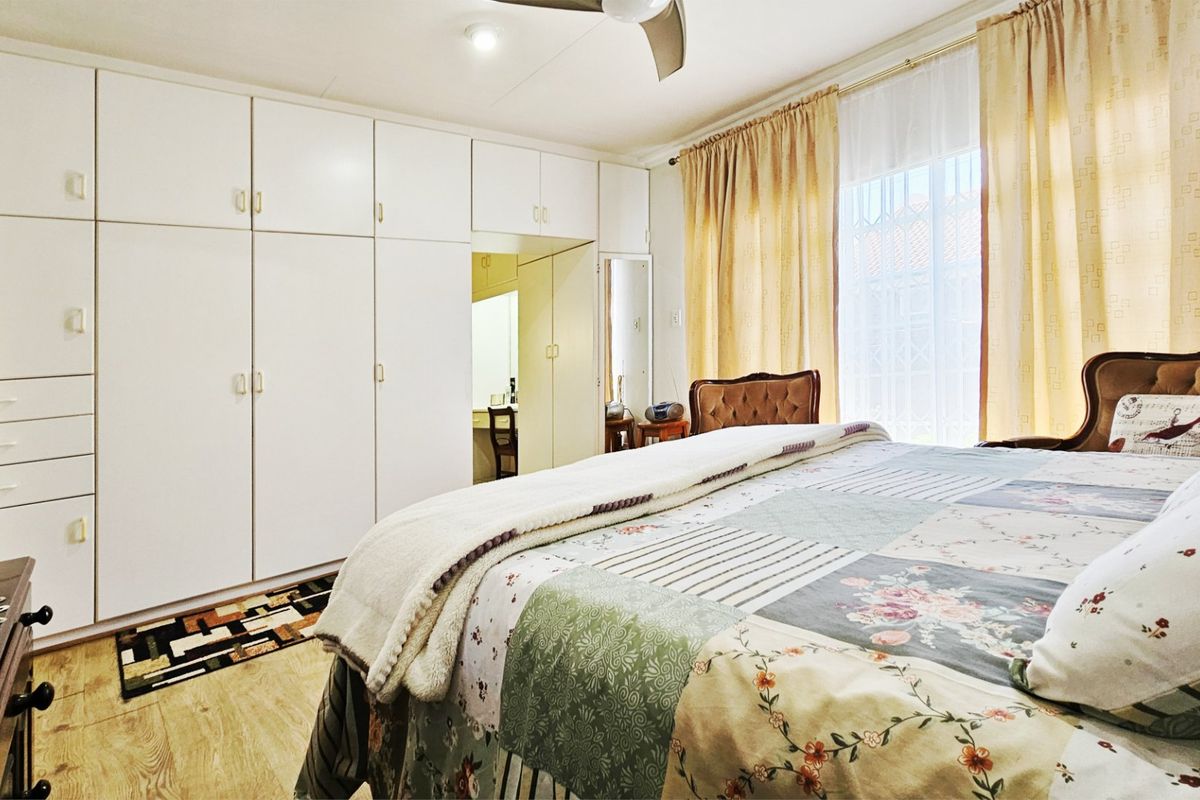 A well-lit bedroom featuring extensive built-in cupboard storage, laminate flooring, and a ceiling fan, offering a functional and comfortable living space.