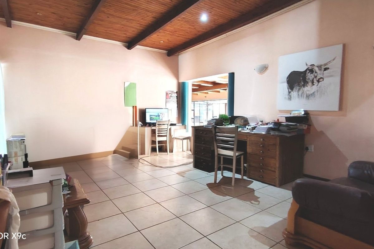 Spacious living area featuring exposed timber beam ceilings, tiled flooring, and an open-plan layout connecting to an adjacent room.