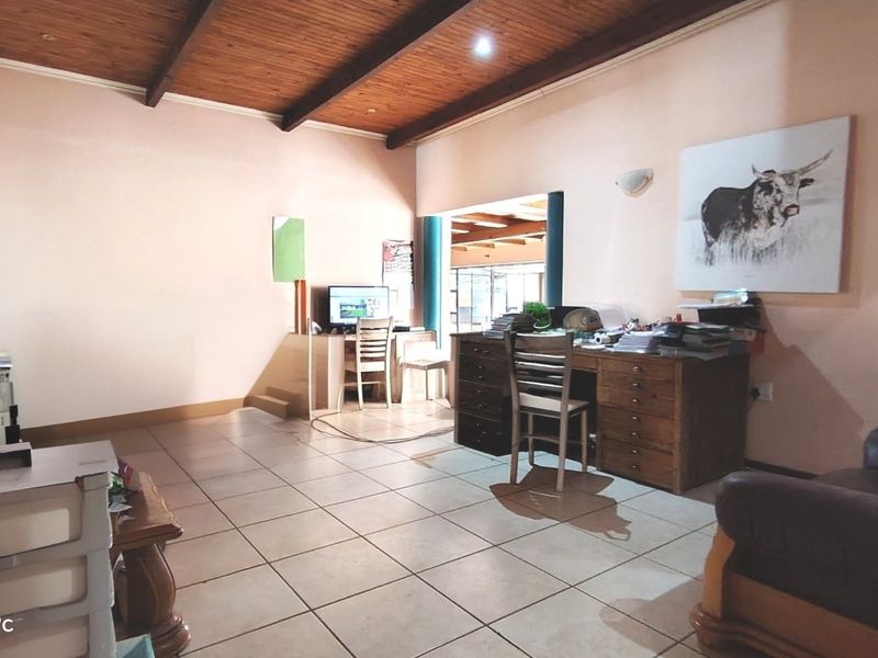 Spacious living area featuring exposed timber beam ceilings, tiled flooring, and an open-plan layout connecting to an adjacent room.