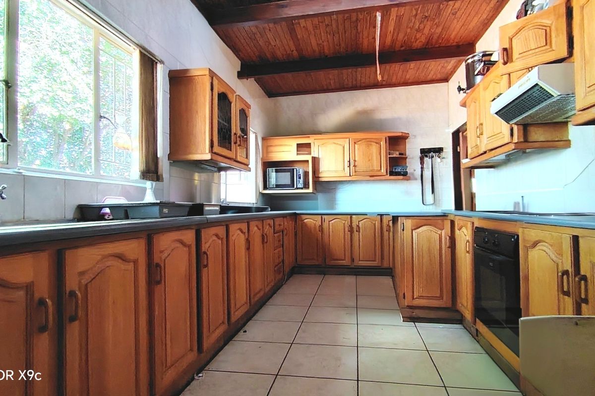 A functional kitchen featuring extensive wooden cabinetry, dark countertops, tiled flooring, and a vaulted timber ceiling with exposed beams.
