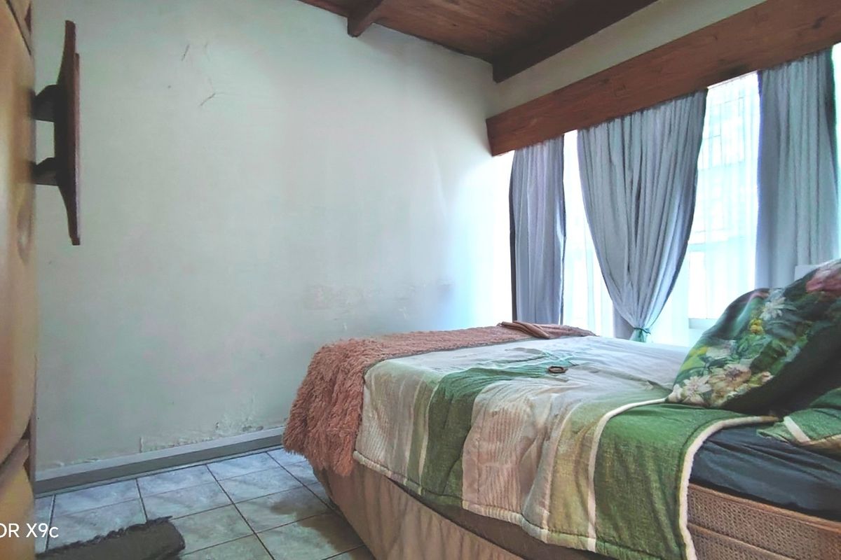 A bedroom featuring exposed timber ceiling beams, tiled flooring, and a window with curtain pelmet.