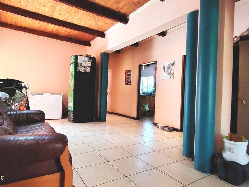 Spacious living area featuring exposed timber beam ceilings, tiled flooring, and decorative structural columns, providing an open-plan layout with access to adjacent rooms.