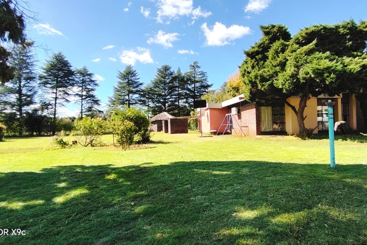 A view of the rear garden and exterior facade of the farm property, featuring established trees and a spacious lawn area.