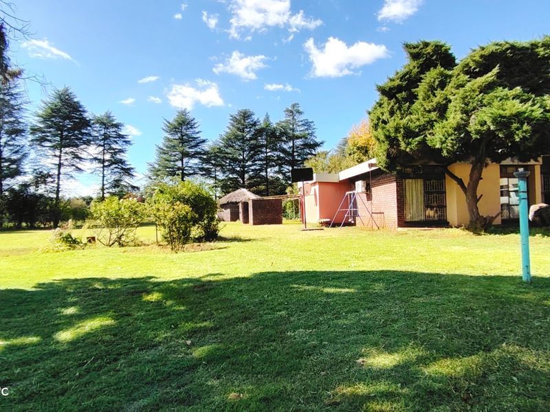 A view of the rear garden and exterior facade of the farm property, featuring established trees and a spacious lawn area.