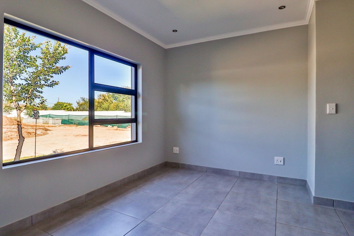 A bright, empty bedroom featuring modern grey floor tiles, neutral walls, and a large aluminium window providing natural light.