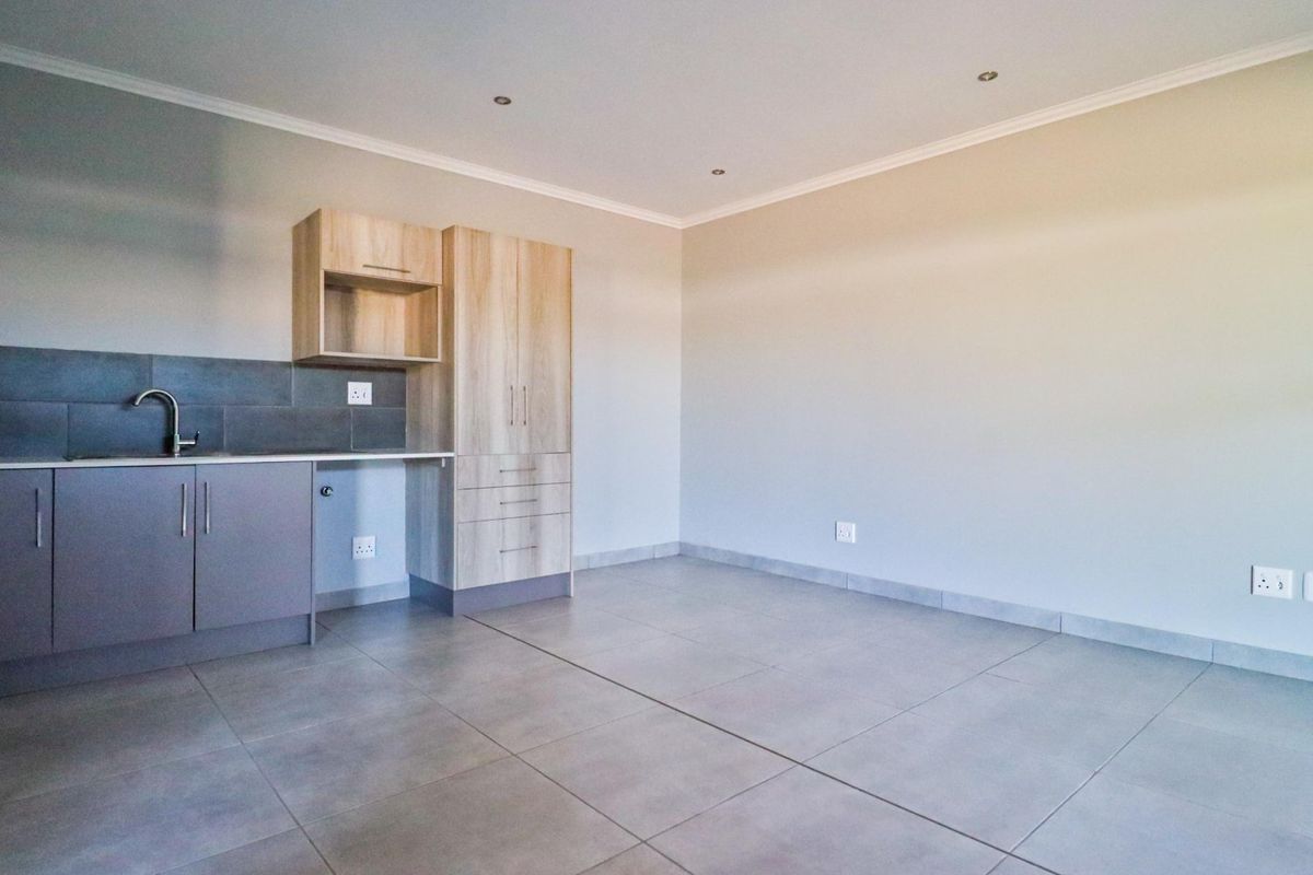 A clean, modern kitchen area featuring neutral cabinetry, tiled flooring, and a functional sink setup, offering a blank canvas for personalization.