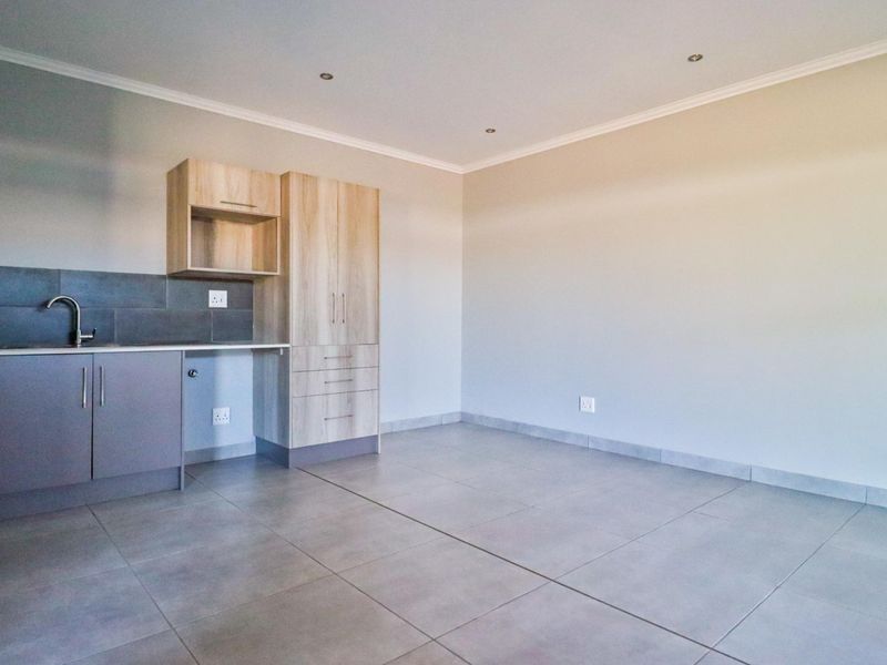 A clean, modern kitchen area featuring neutral cabinetry, tiled flooring, and a functional sink setup, offering a blank canvas for personalization.