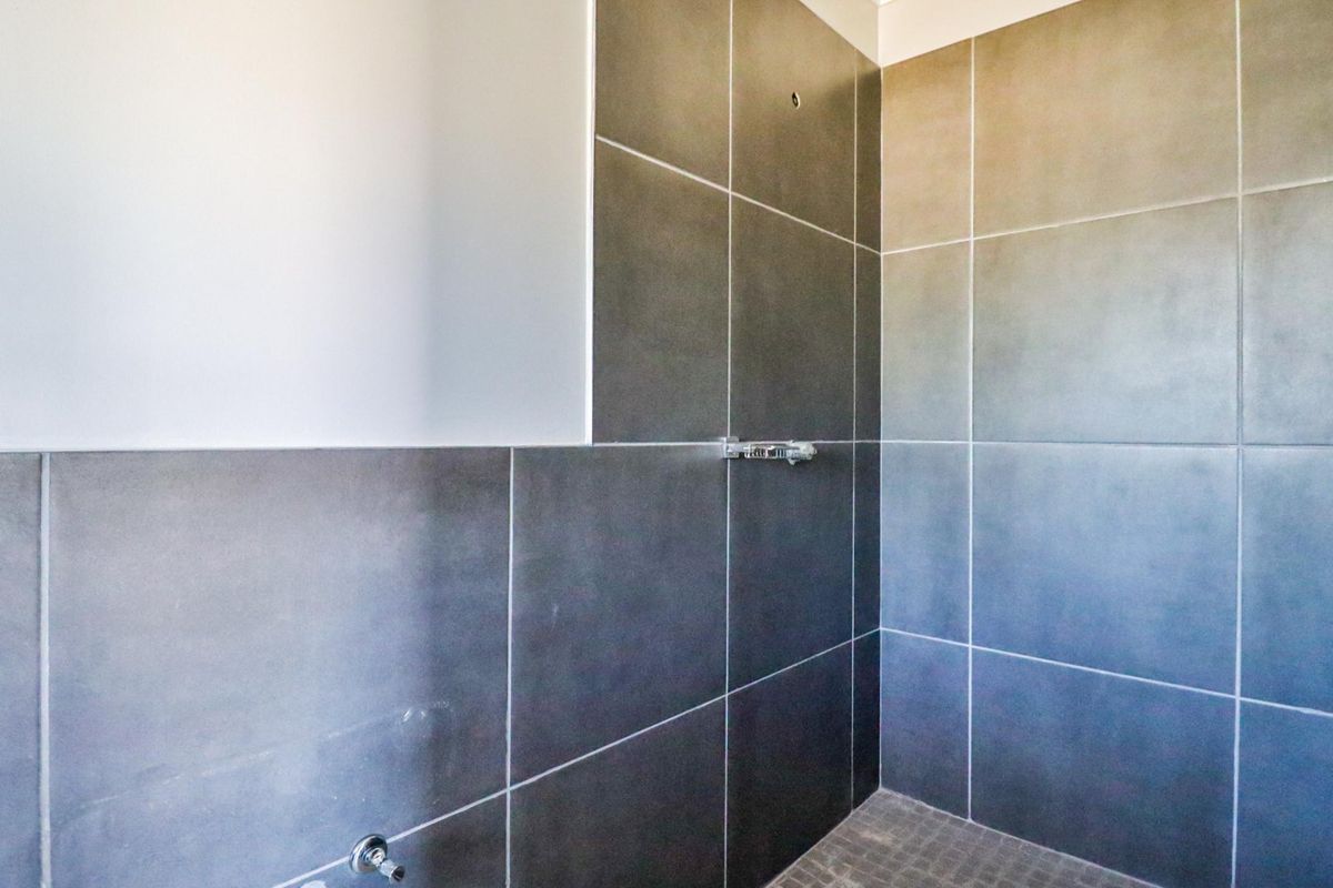A shower enclosure featuring large format grey wall tiles and mosaic floor tiles, currently requiring a shower head and finishing touches to the wall tiling.