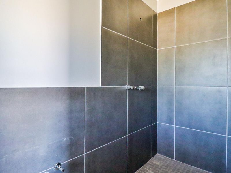 A shower enclosure featuring large format grey wall tiles and mosaic floor tiles, currently requiring a shower head and finishing touches to the wall tiling.