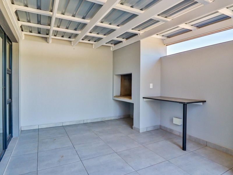 Covered patio area featuring a built-in braai, tiled flooring, and a fixed counter, providing a functional outdoor entertainment space.