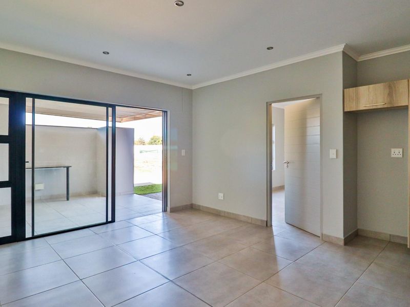 A bright, modern open-plan living area featuring neutral tiled floors, recessed lighting, and seamless access to an outdoor patio through large sliding glass doors.