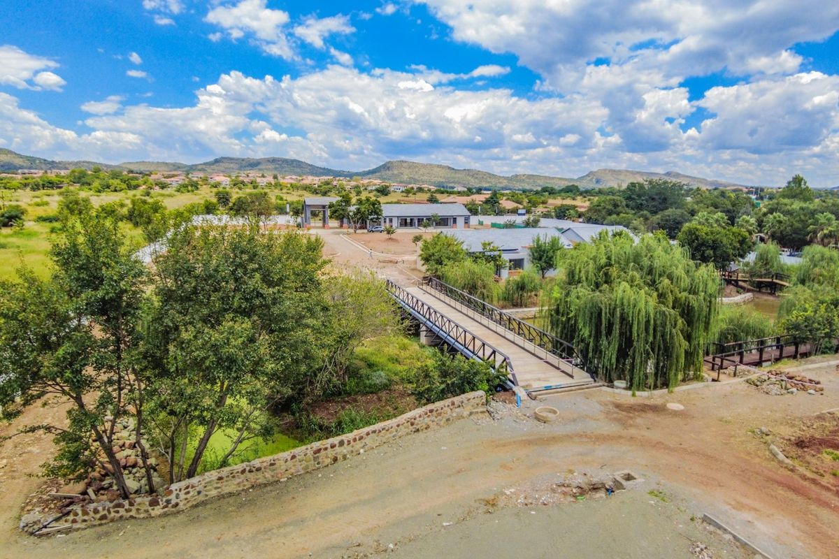 Aerial view of the estate grounds featuring a pedestrian bridge, landscaped surroundings, and established trees within a scenic residential setting.
