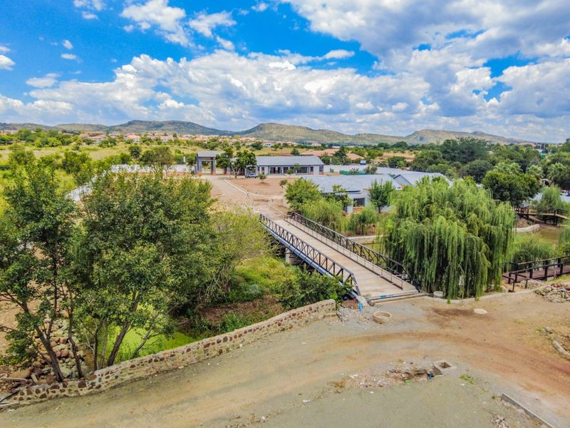 Aerial view of the estate grounds featuring a pedestrian bridge, landscaped surroundings, and established trees within a scenic residential setting.