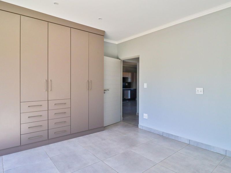 A clean, empty bedroom featuring neutral tiled flooring, built-in cupboards with integrated drawers, and recessed downlighting.
