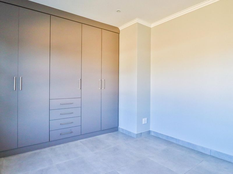 A clean, empty bedroom featuring modern built-in cupboards, neutral tiled flooring, and crisp finishes, ready for personalization.