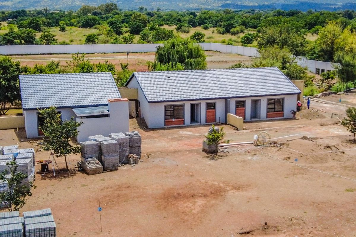Aerial view of a townhouse development under construction, featuring tiled roofs, brick accents, and expansive surrounding grounds.
