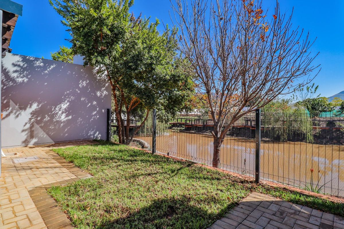 A private rear garden featuring a paved patio area, lawn, and secure fencing overlooking a tranquil water feature.