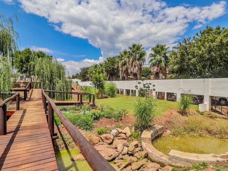 A landscaped garden area featuring a wooden footbridge, stone water feature, and perimeter wall with electric fencing.