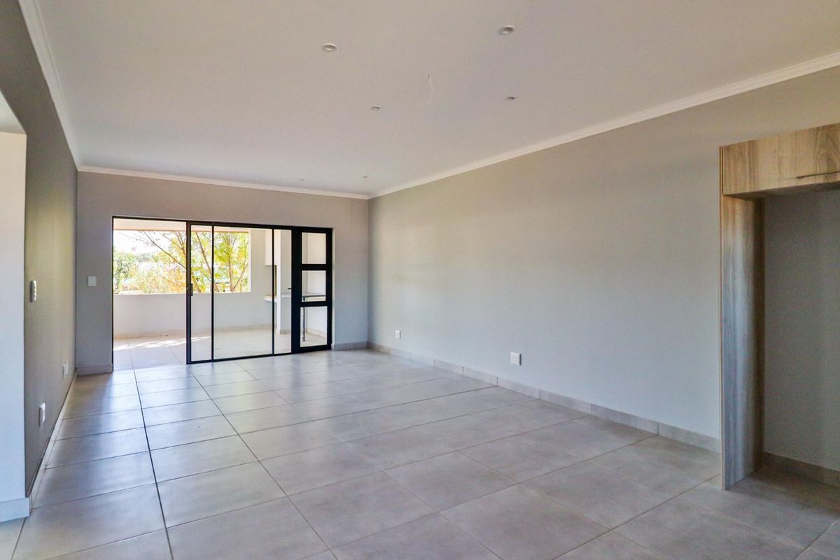 Spacious, empty living area featuring neutral tiled flooring, recessed lighting, and a large sliding glass door providing access to an outdoor patio.