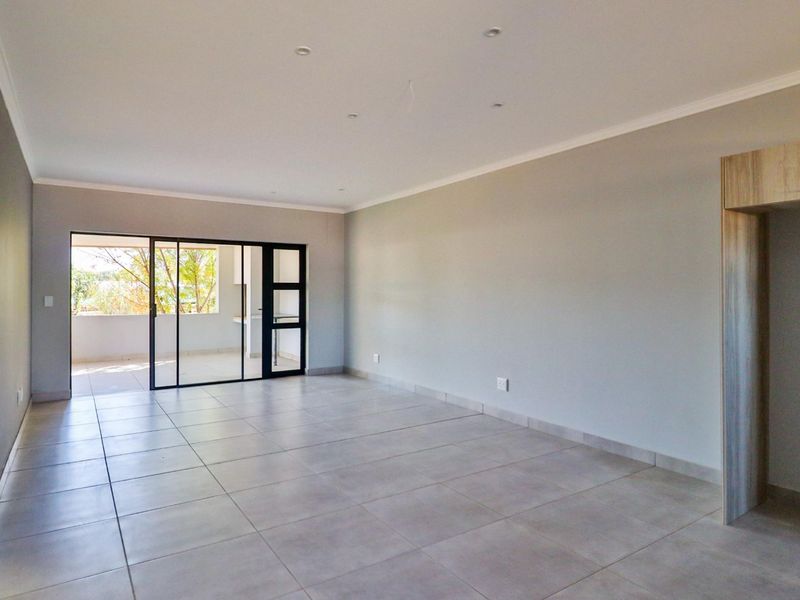 Spacious, empty living area featuring neutral tiled flooring, recessed lighting, and a large sliding glass door providing access to an outdoor patio.