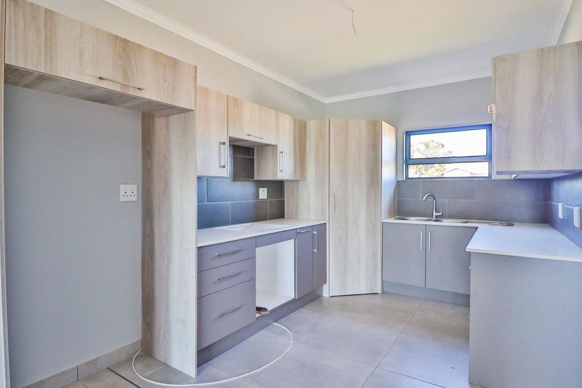 A modern, empty kitchen featuring light wood-tone cabinetry, grey tiled backsplash, and neutral floor tiles, offering a clean and functional space.